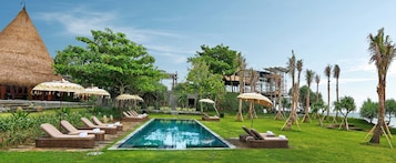 Zona junto a la piscina con sillas de descanso y sombrillas, rodeada de vegetación y vistas al mar.