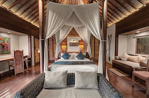 A spacious room with a large bed, a wooden floor, a window with a view, and a ceiling with a thatched design.