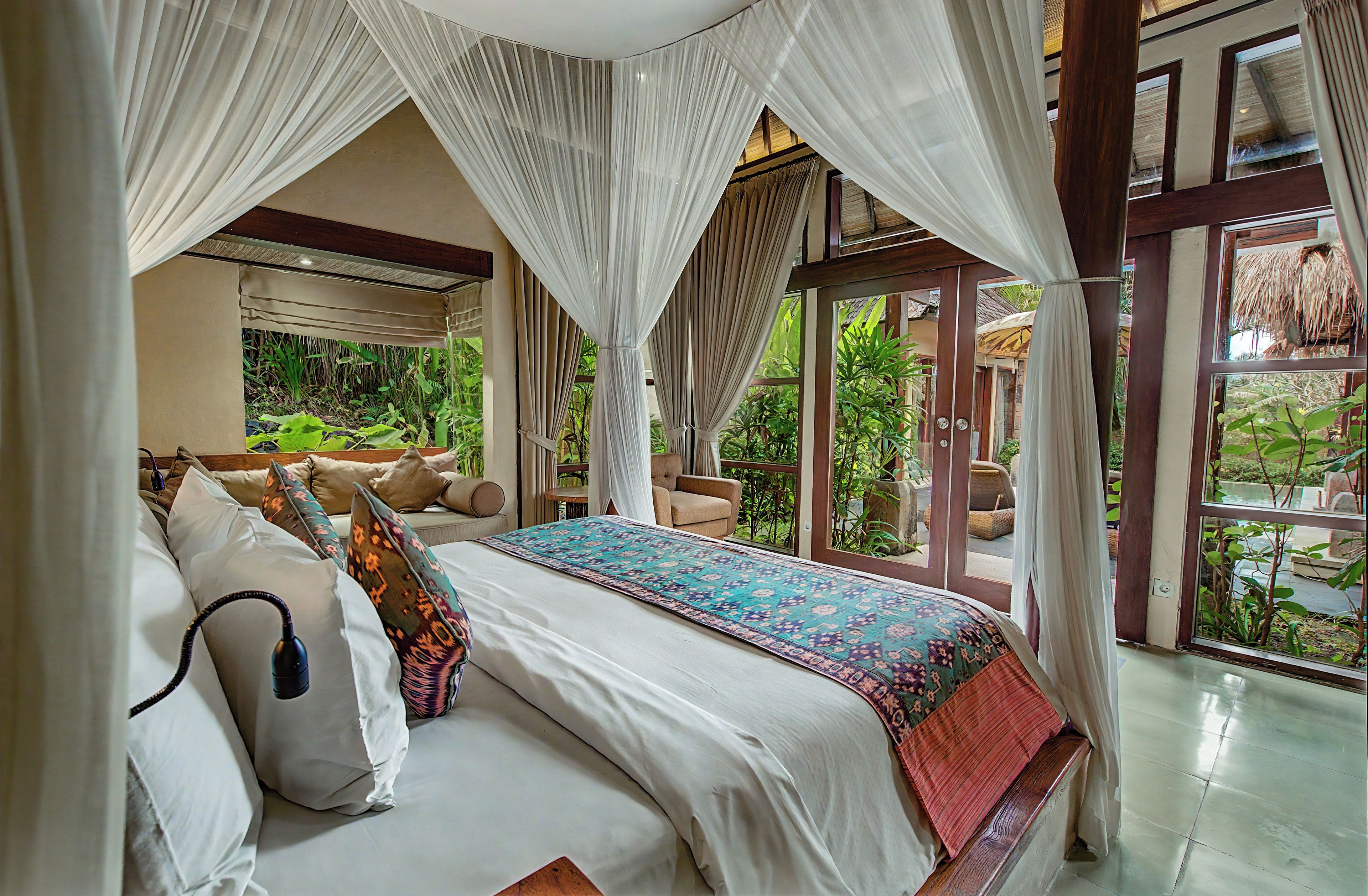 A bedroom with a canopy bed, a view of greenery outside, and a large window.