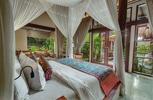 A bedroom with a canopy bed, a view of greenery outside, and a large window.