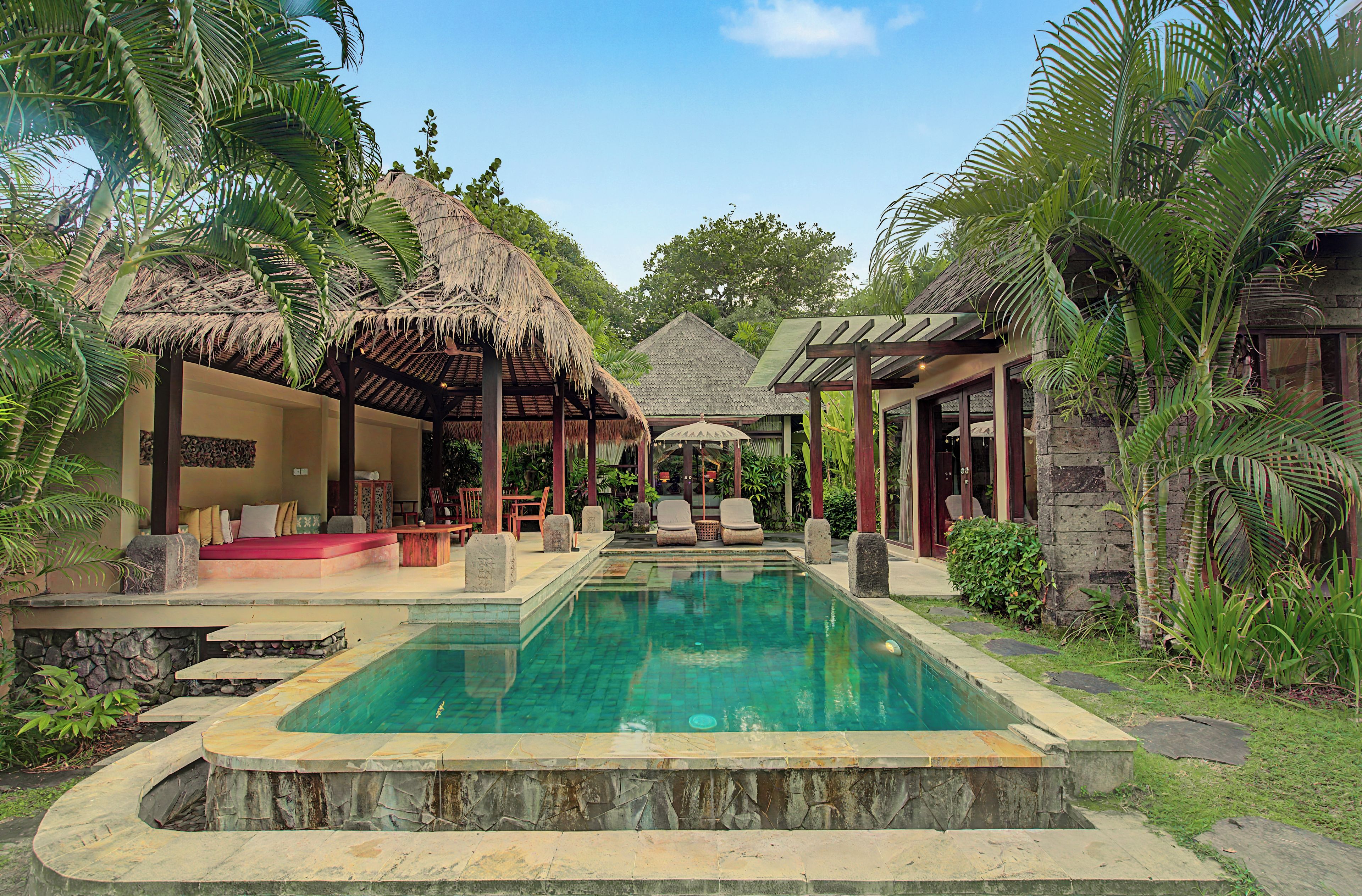A pool area with a thatched-roof structure, lounge chairs, and a stone wall.