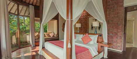A spacious bedroom with a four-poster bed, a sitting area with a sofa, and a large window providing a view of the outdoors.