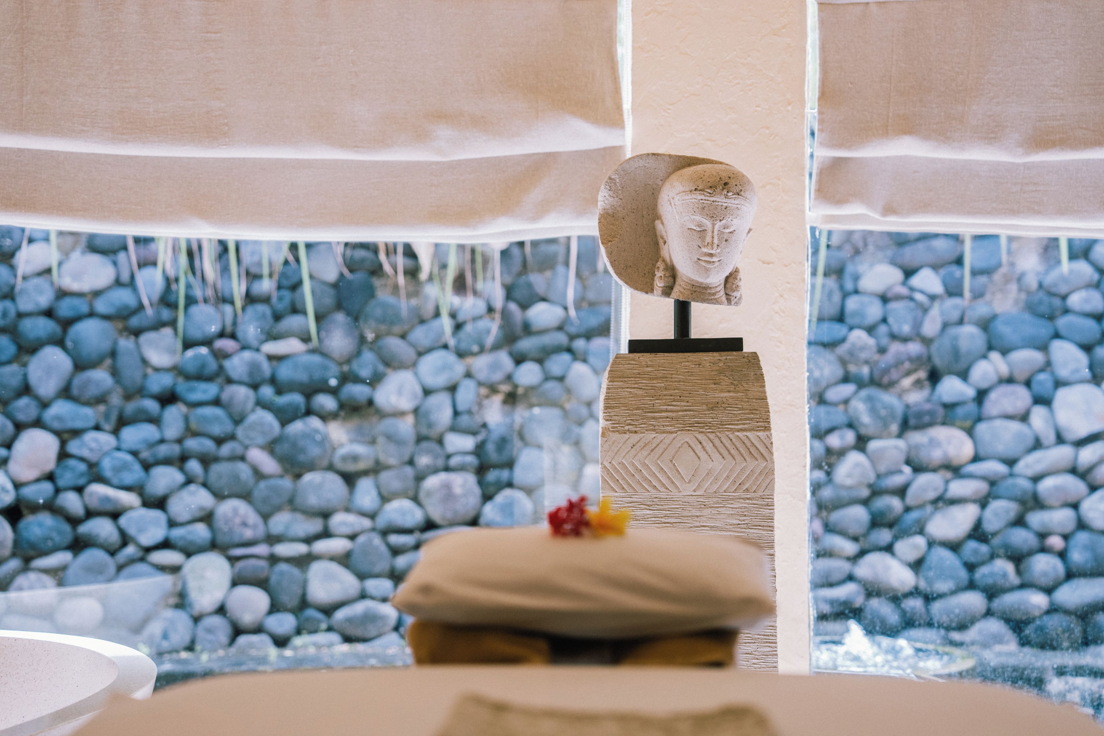 Un área de spa con un fondo de pared de piedra, una escultura de piedra y un banco de madera con cojín.