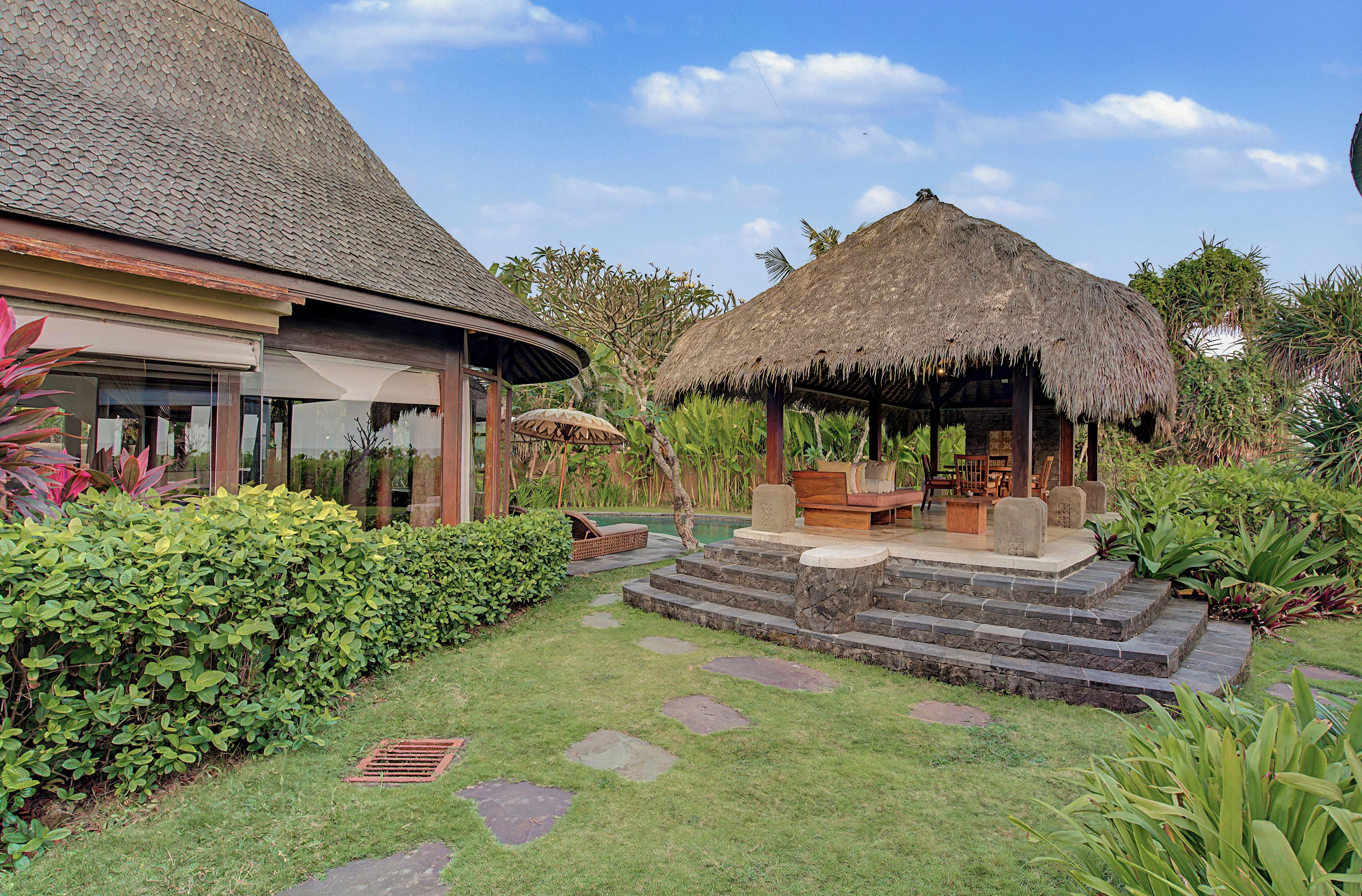 A tropical resort with thatched-roof structures, a pool, and lush greenery.