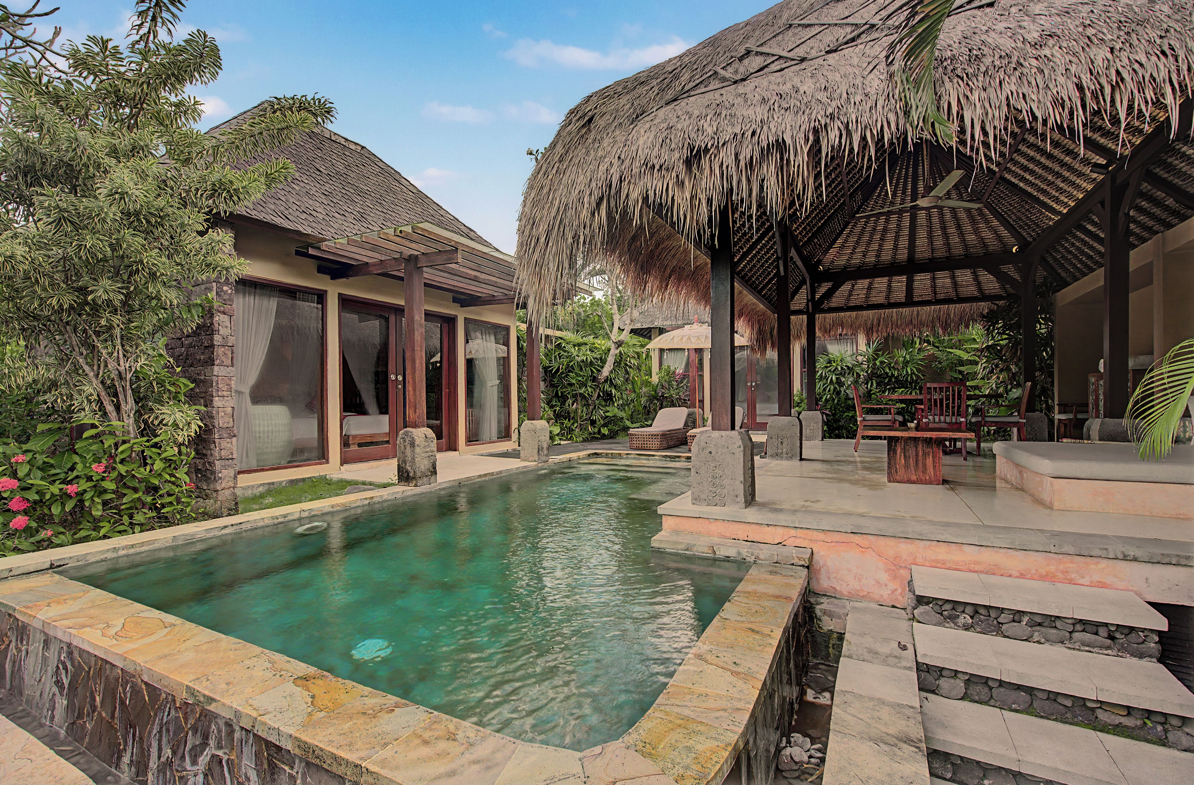A pool area with a clear water surface, surrounded by a stone deck and a thatched-roof structure.