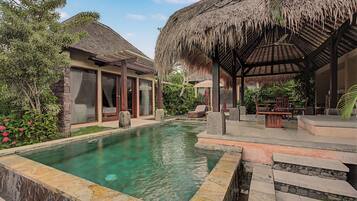 A pool area with a clear water surface, surrounded by a stone deck and a thatched-roof structure.