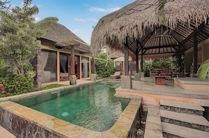 A pool area with a clear water surface, surrounded by a stone deck and a thatched-roof structure.