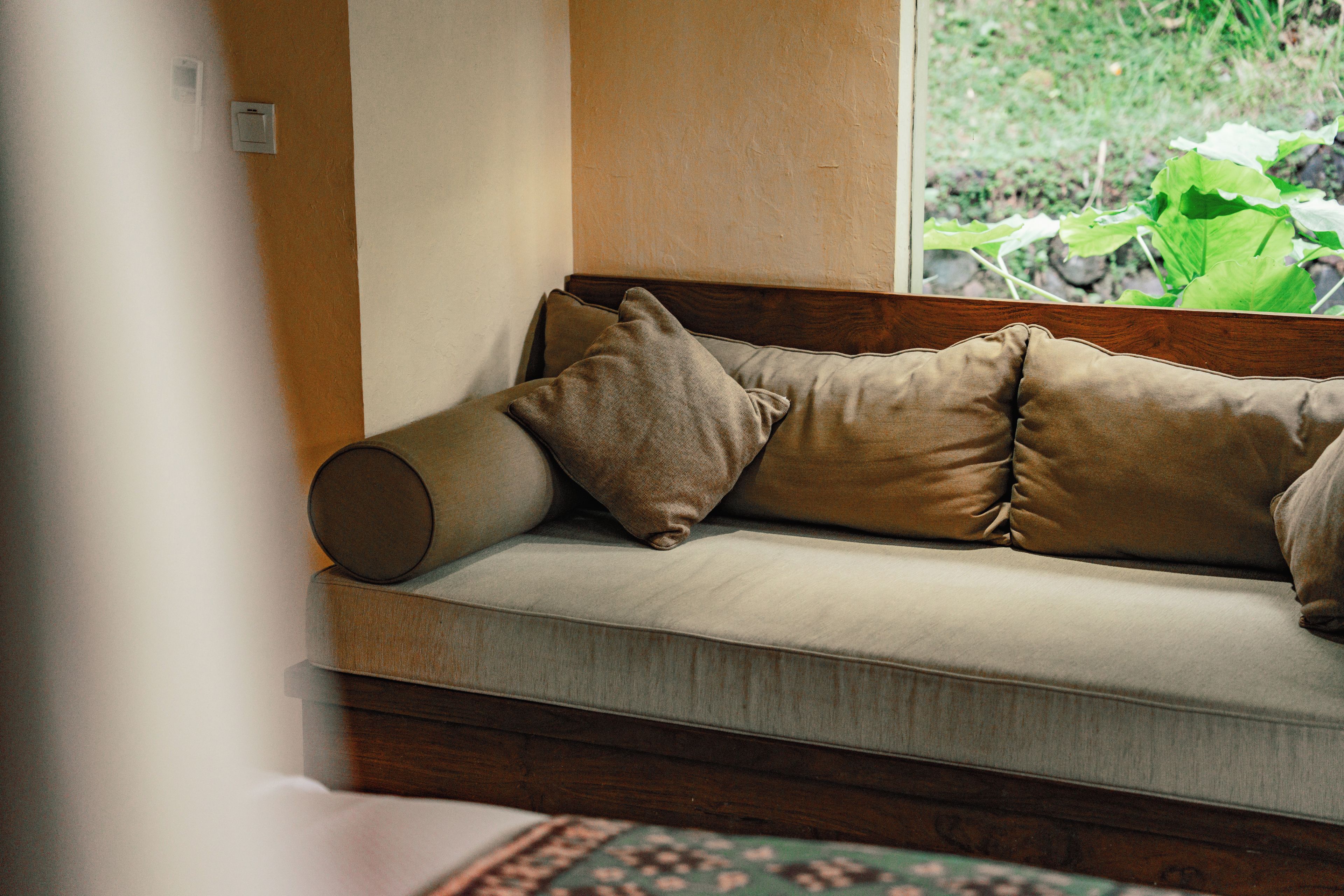 A sofa with multiple cushions in a room with a window.