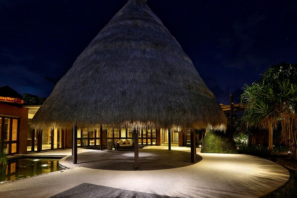 A thatched-roof structure with a pool and lounge area, surrounded by palm trees and a night sky. - WakaGangga (Tabanan)