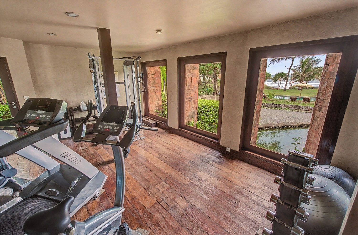 A gym with exercise equipment, large windows, and a view of a landscaped area.