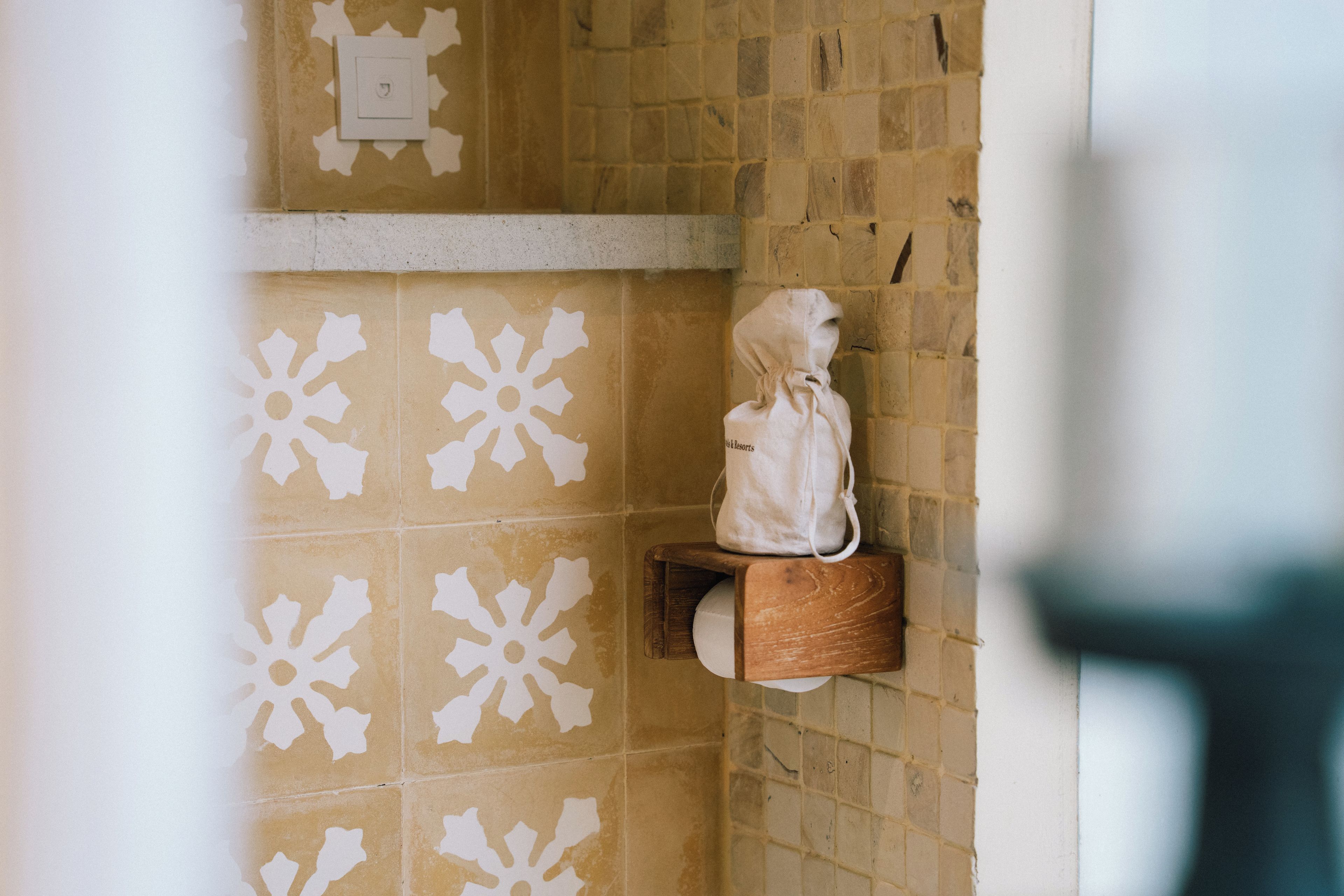 A bathroom with patterned tiles, a towel rack, and a bag hanging on it.