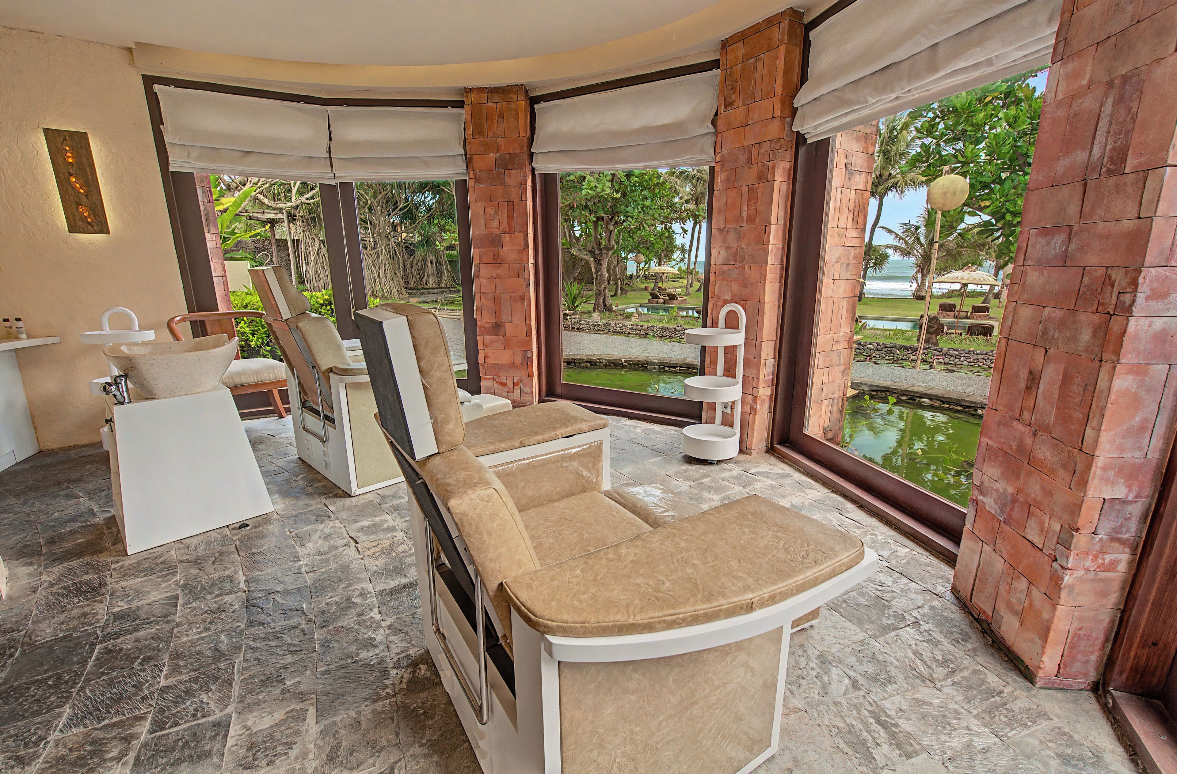 A spa room with a massage table, chairs, a small pool, and a view of the ocean.
