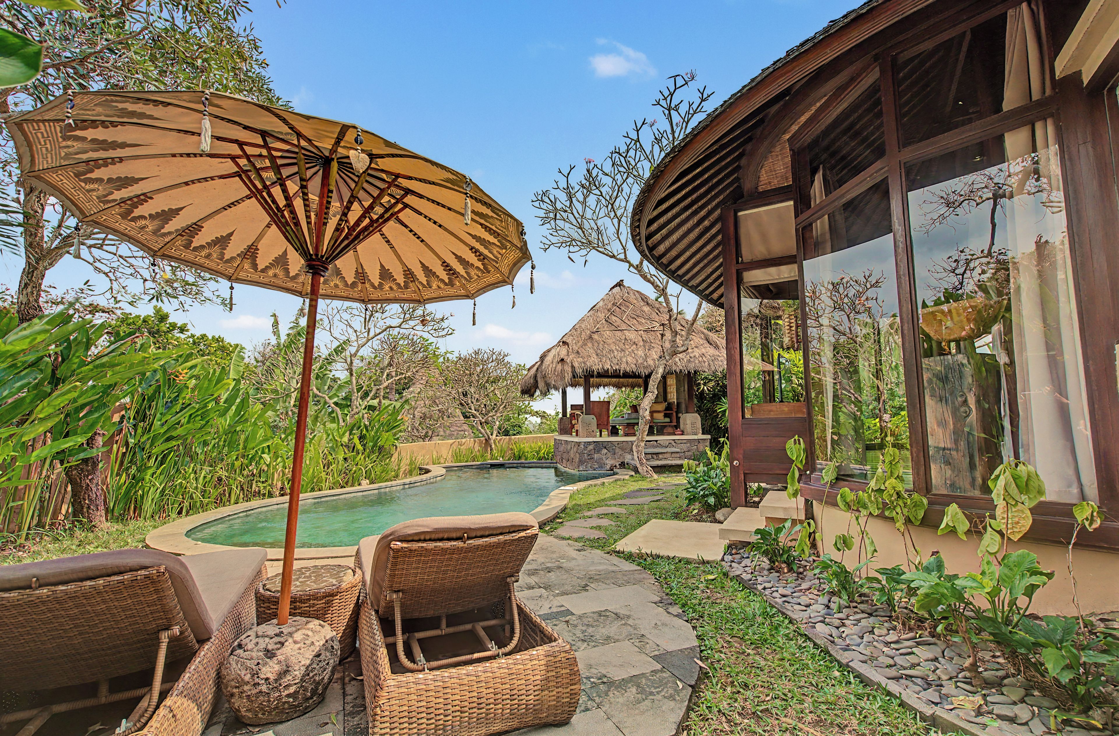 A pool area with lounge chairs, a thatched-roof structure, and a building with large windows.