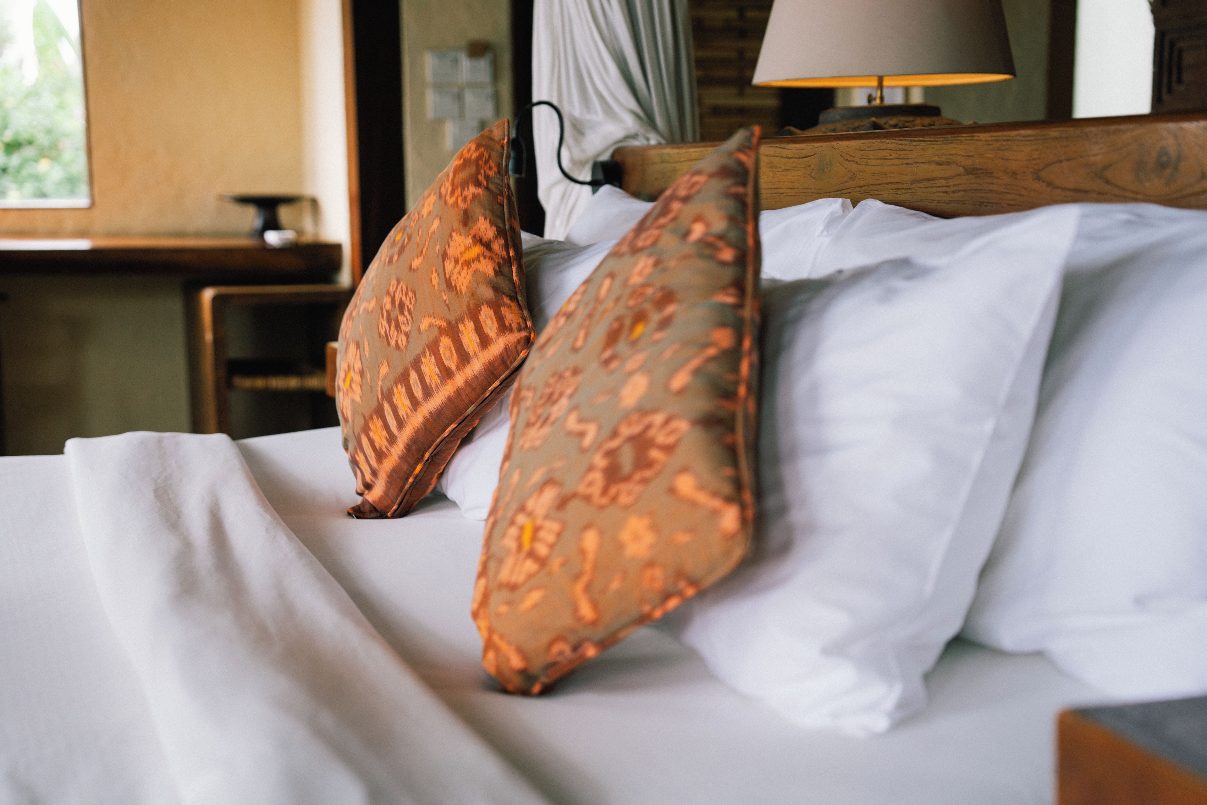 Una cama con sábanas blancas y dos almohadas estampadas.