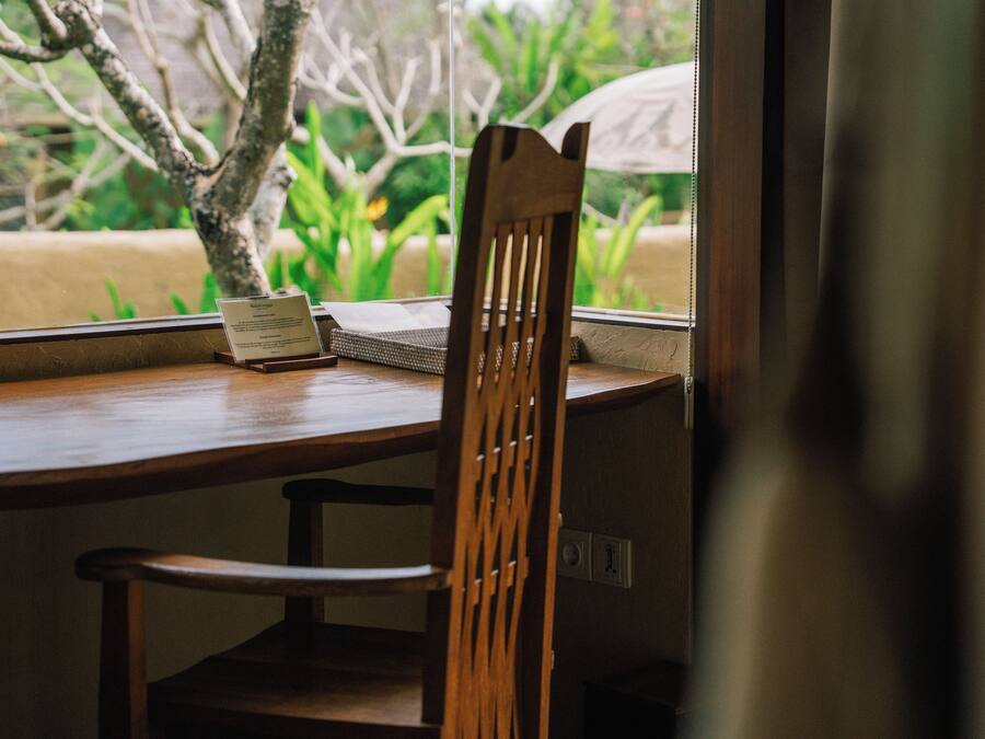 Una mesa de madera con una silla, un letrero pequeño y una ventana que da a zonas verdes.