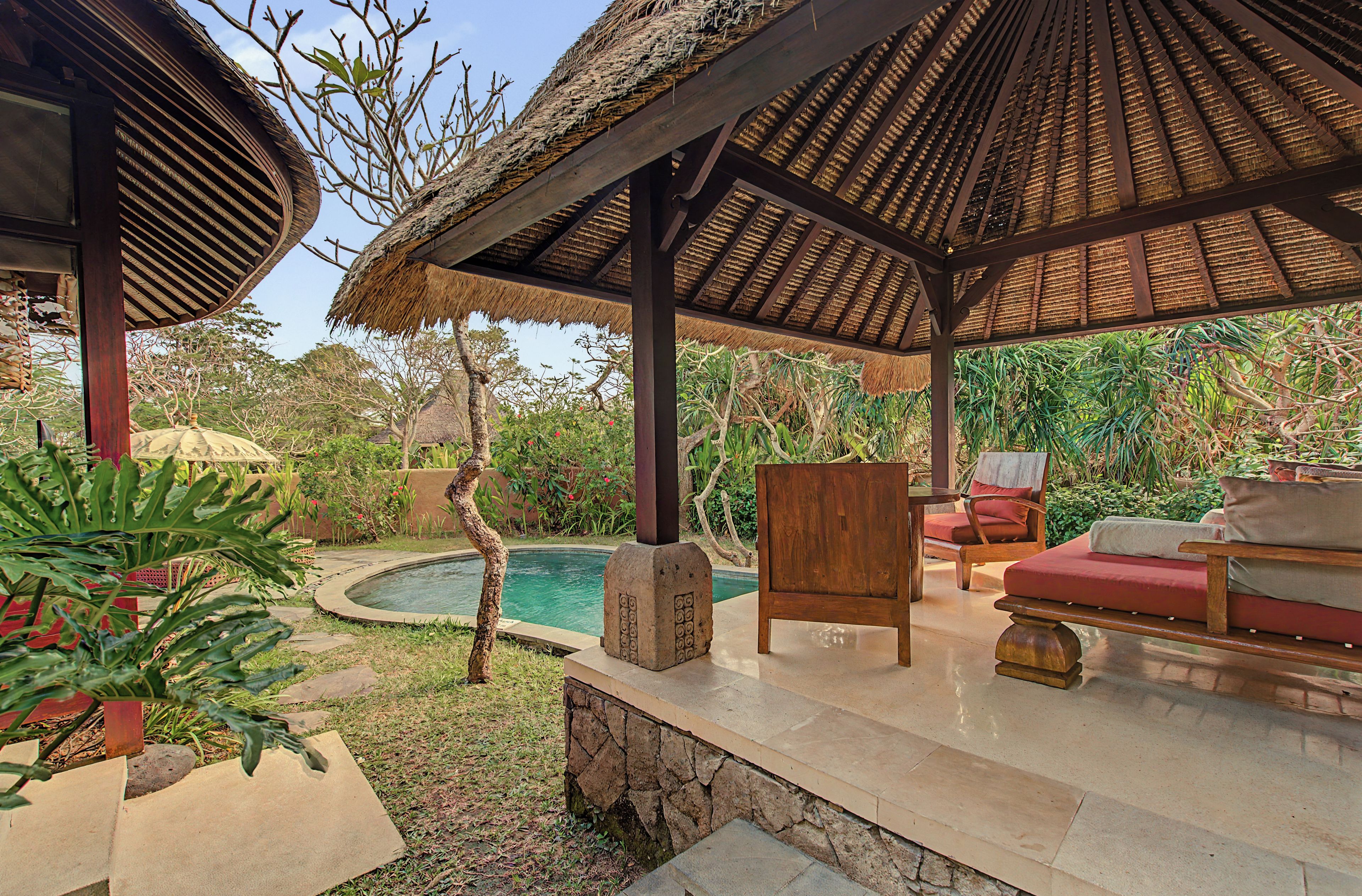 A covered outdoor area with a pool, seating, and tropical plants.