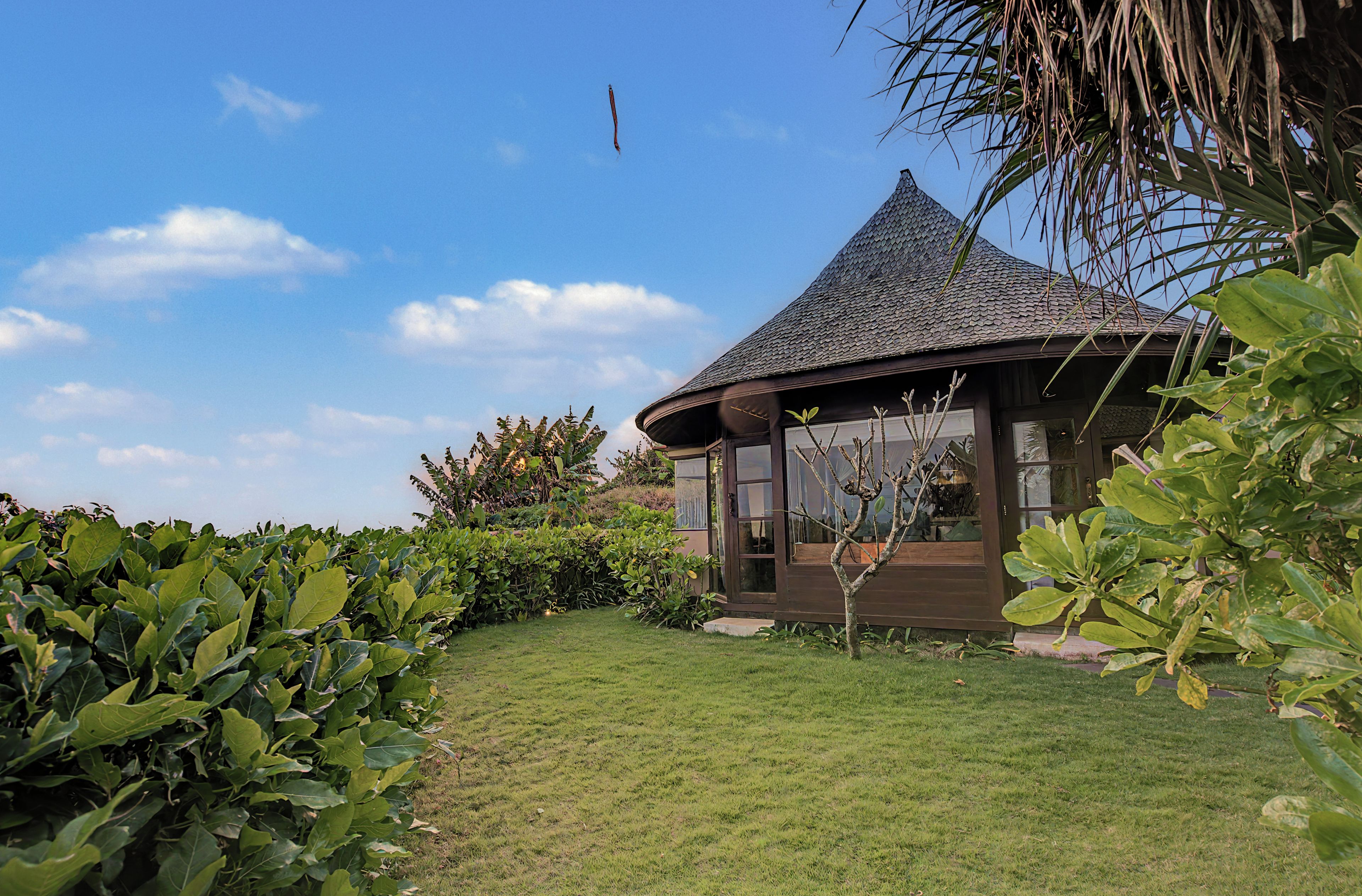 Ein Kiosk mit einem Ziegeldach, umgeben von üppiger Vegetation und blauem Himmel.