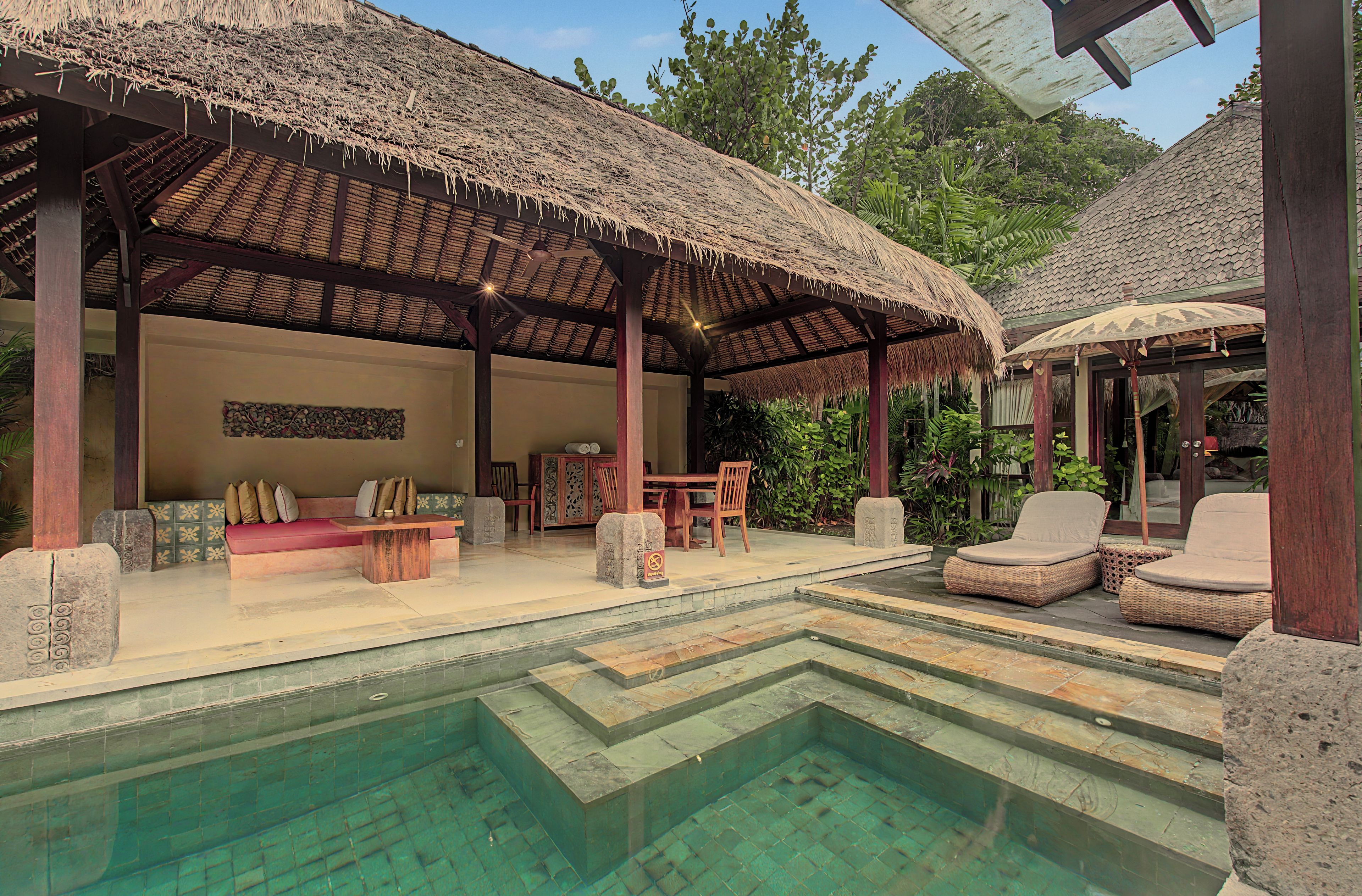 Área junto a la piscina con techo de paja, asientos y piscina de piedra.