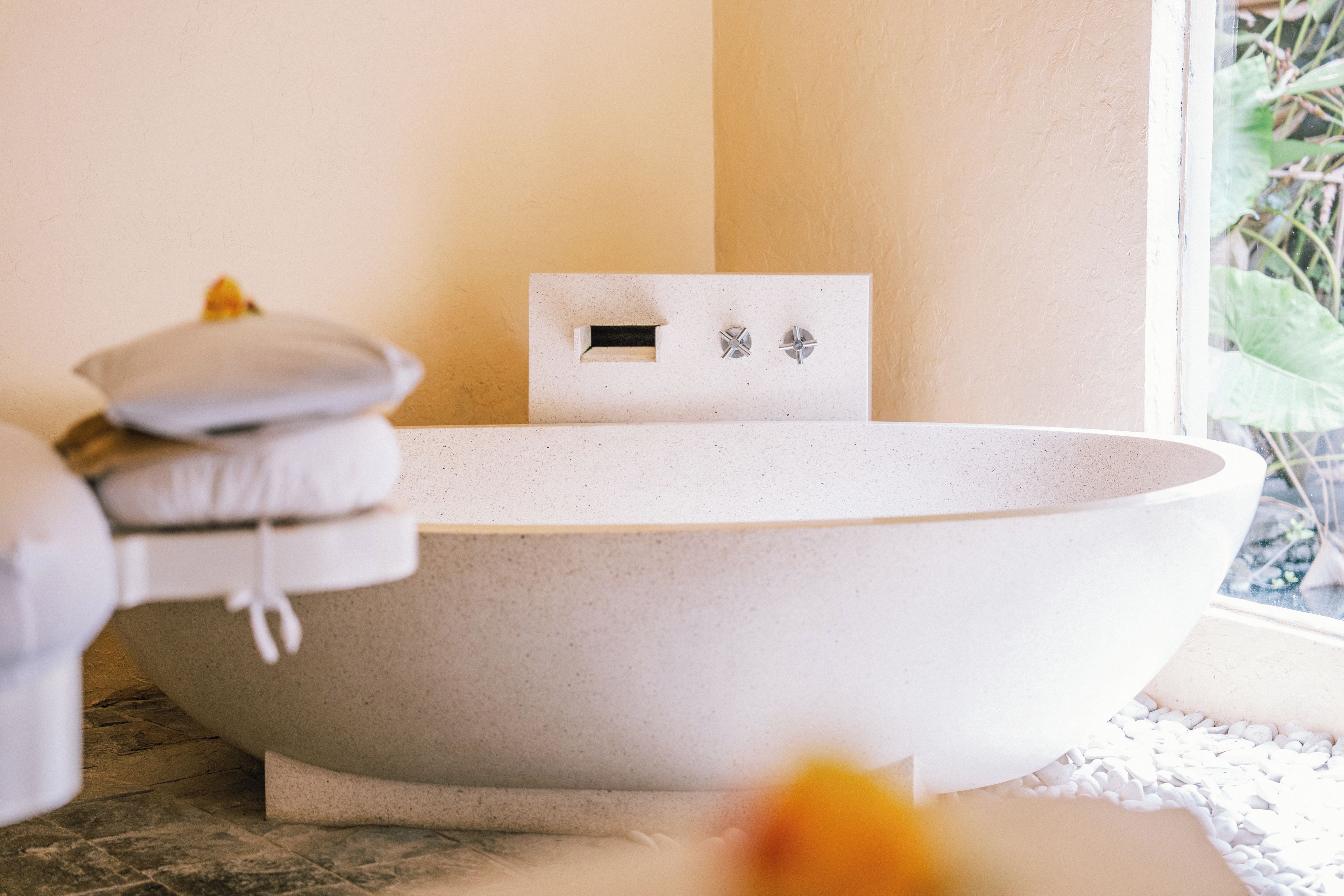Una bañera con un panel de ducha rectangular, un perchero y una planta en un baño.