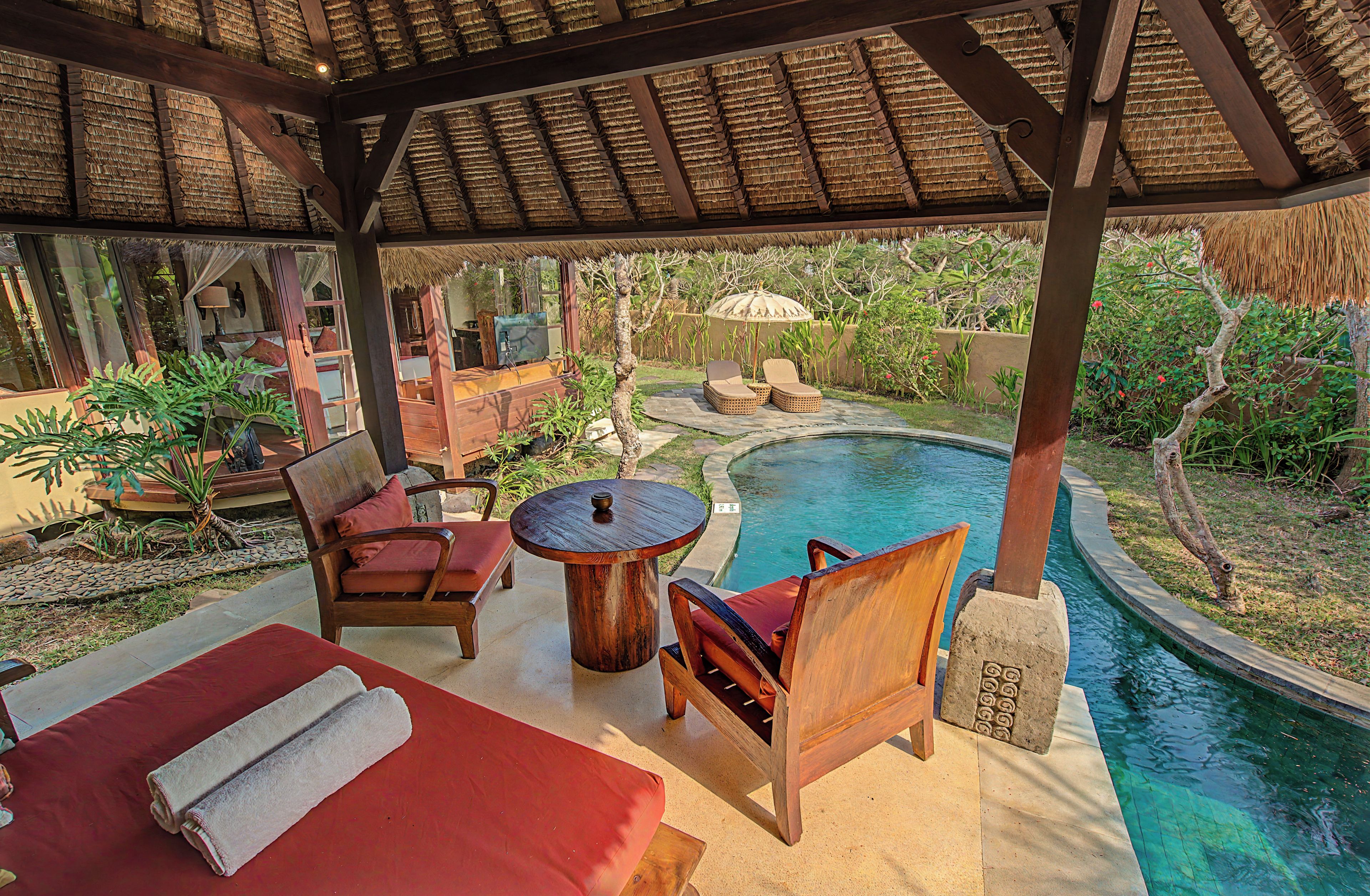A covered outdoor seating area with a pool, lounge chairs, and a table.