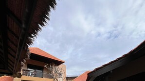 A courtyard with a stone pathway, a thatched-roof structure, and a building with a red-tiled roof. - Visakha Sanur by Puri Signatures (Denpasar)