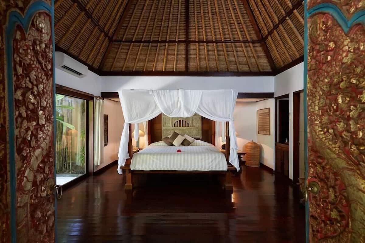 A spacious room with a large bed, a thatched roof, and a view of greenery outside.