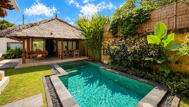 A swimming pool with a thatched-roof structure, surrounded by lush greenery and a bamboo fence. - Visakha Sanur by Puri Signatures (Denpasar)