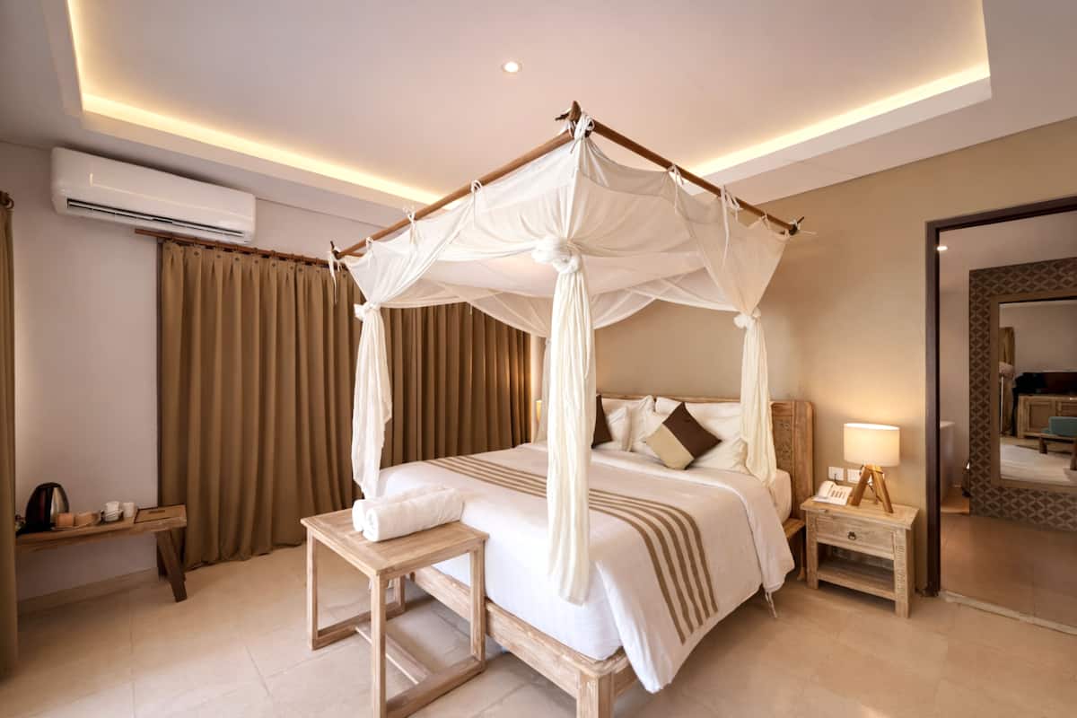 A four-poster canopy bed with a bedside table and lamp, a wooden nightstand, and a mirror on the wall.
