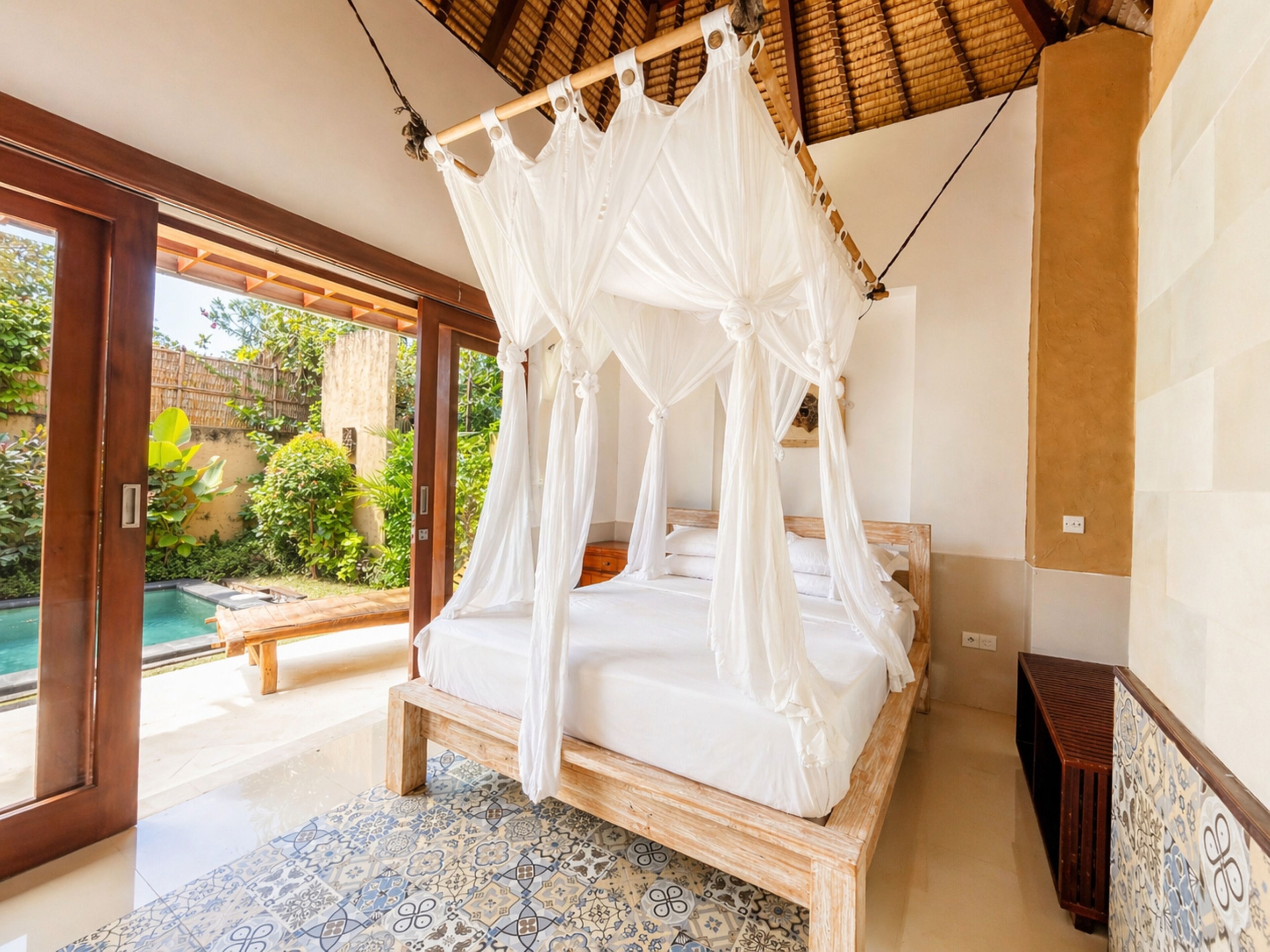 Un dormitorio con cama con dosel, vistas a una piscina y suelo de baldosas.