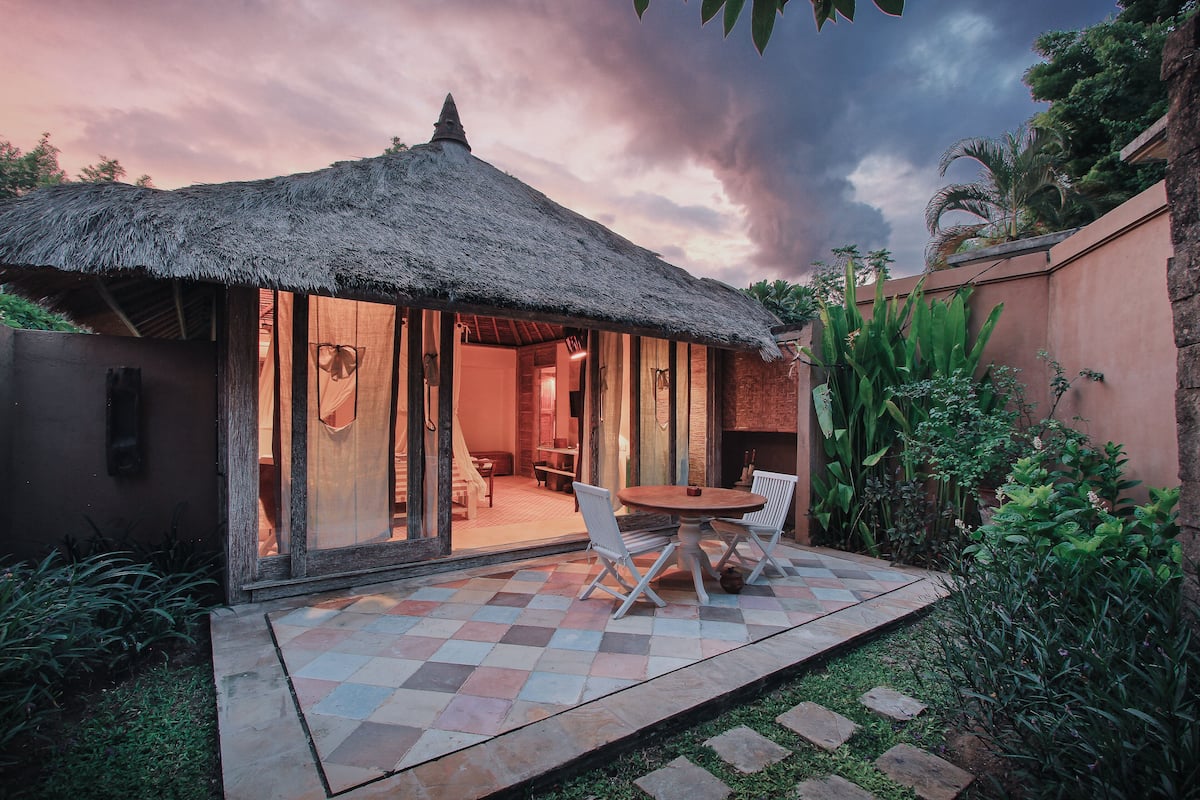 A thatched-roof structure with a checkered patio, white chairs, and a table.