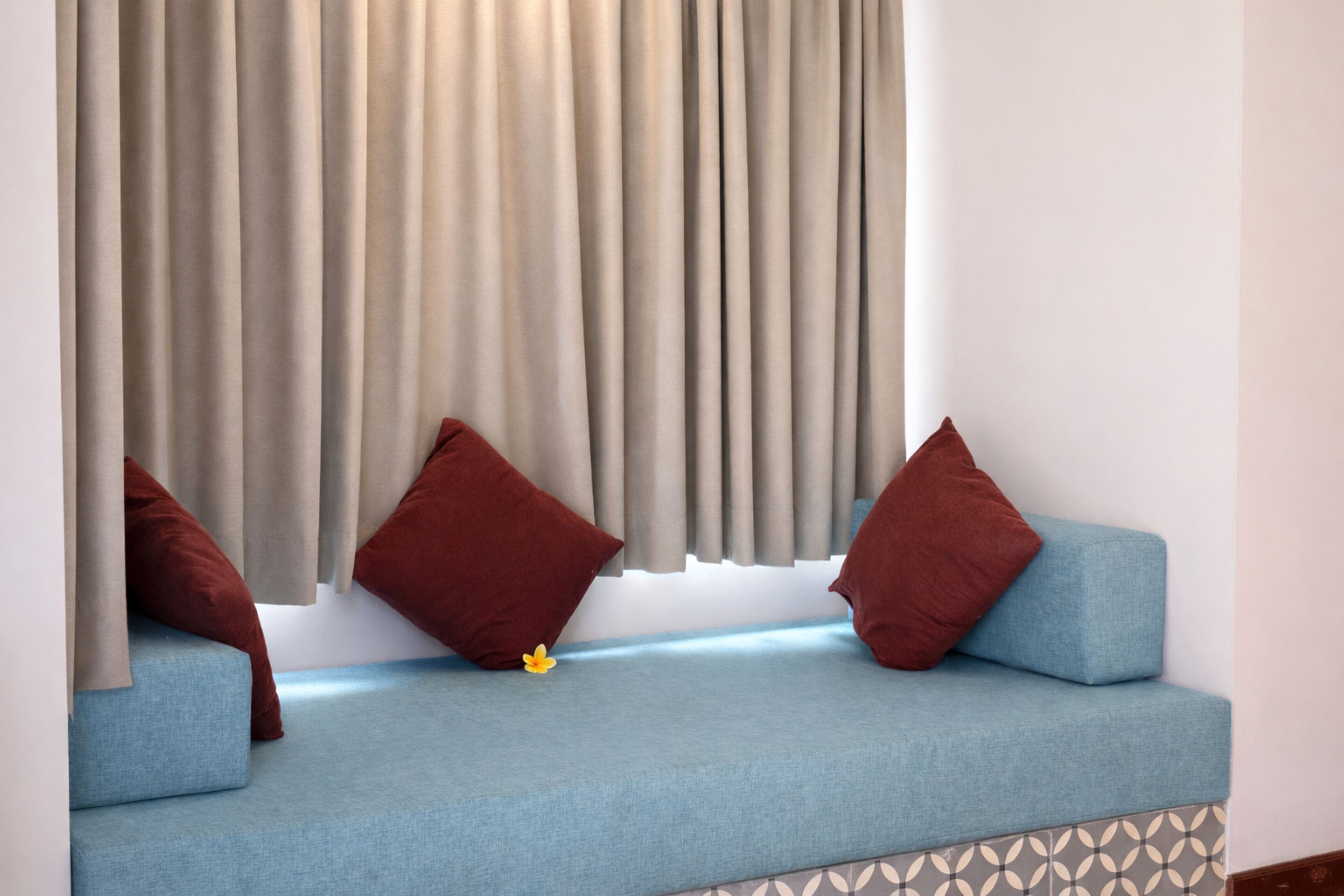 Una habitación con un sofá azul, cortinas color beige y una pequeña flor amarilla.