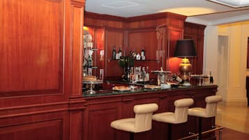 A bar area with wooden paneling, a counter with various bottles and glasses, and three bar stools.