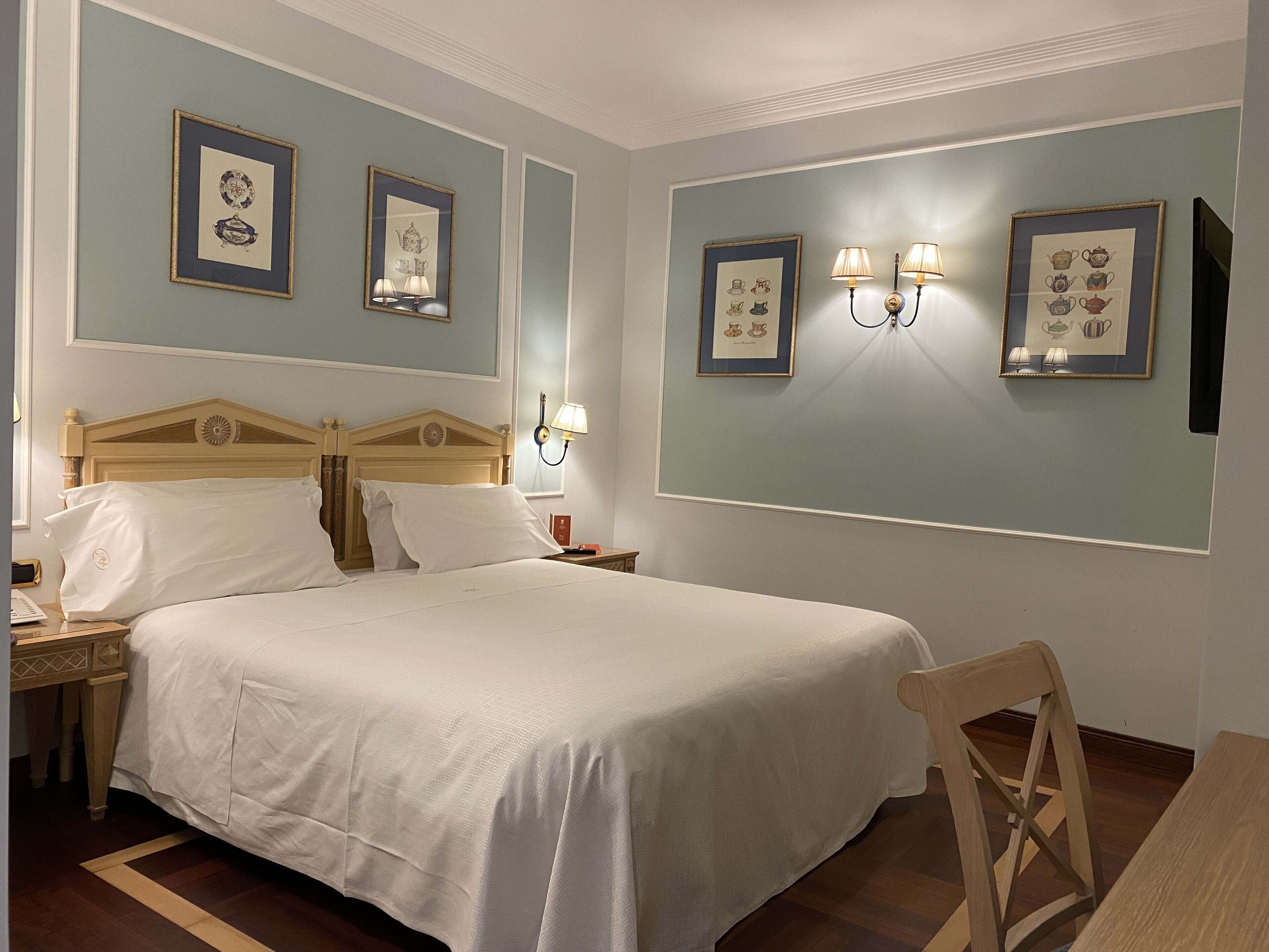 Una camera d'albergo ordinata con un letto grande, un comodino in legno, un tavolino e una sedia.