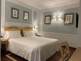 Una camera d'albergo ordinata con un letto grande, un comodino in legno, un tavolino e una sedia.