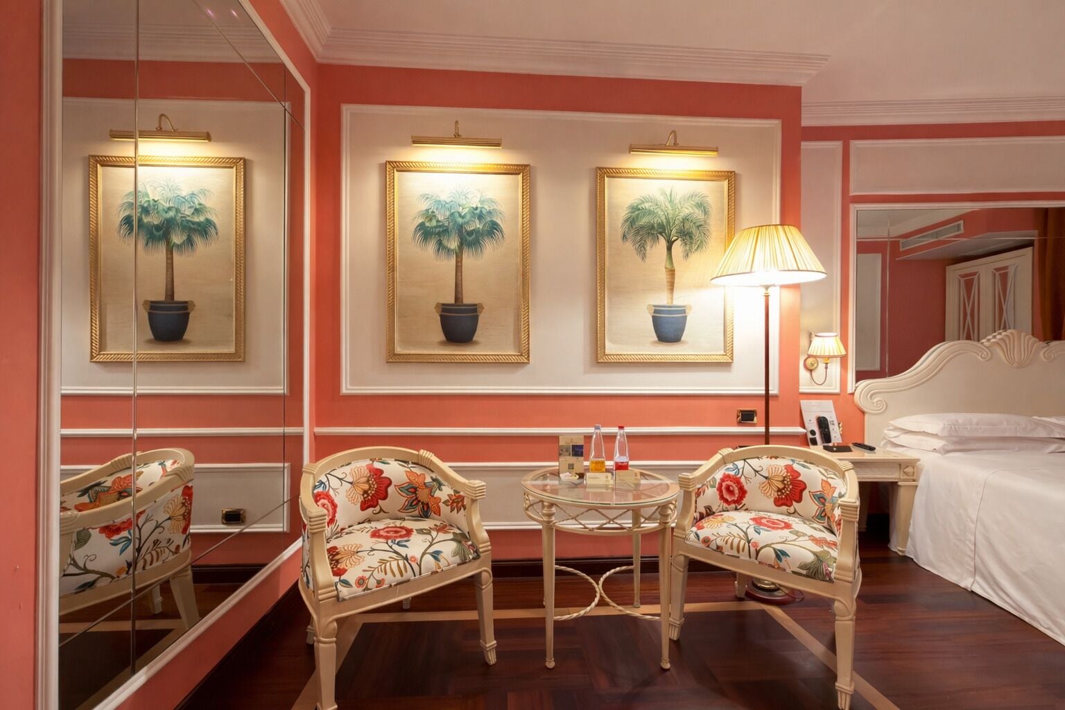 Habitación de hotel con una cama, dos sillas, una mesa redonda pequeña y tres cuadros en la pared.