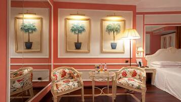 A hotel room with a bed, two chairs, a small round table, and three framed paintings on the wall.