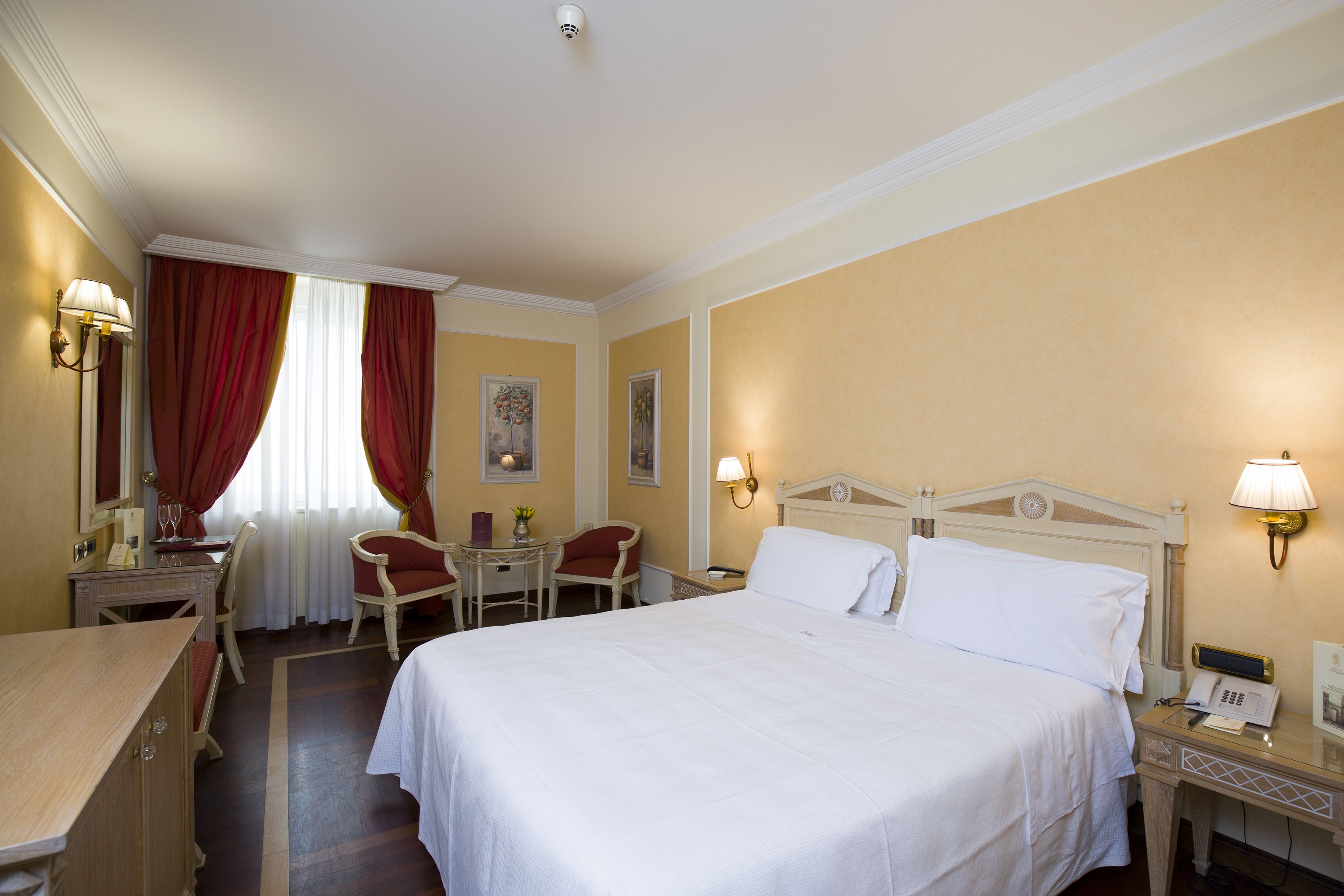 Una camera d'albergo con un letto grande, una scrivania, una sedia, un tavolino e due lampade.