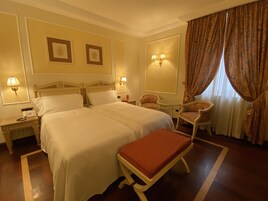 Camera d'albergo con un letto grande, due comodini, una sedia, un tavolino e una finestra con tende.