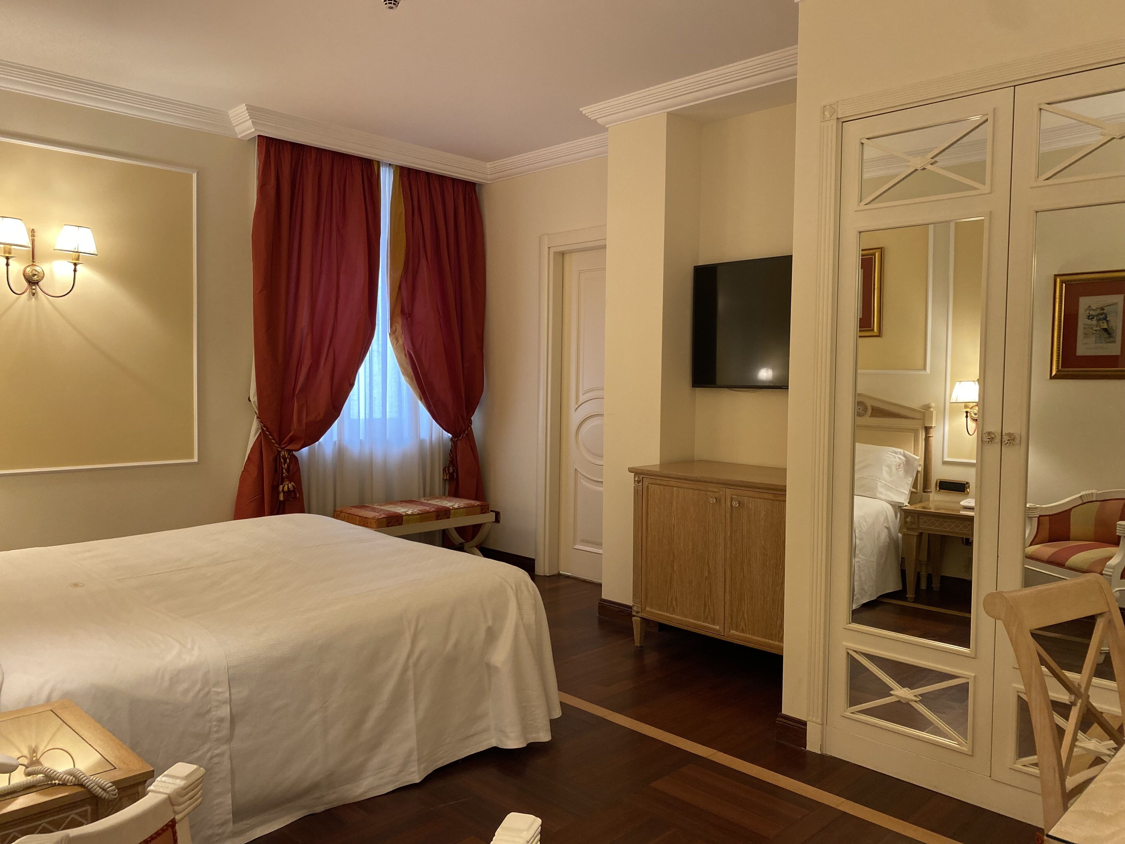 Una habitación de hotel con cama, escritorio, televisor y espejo.