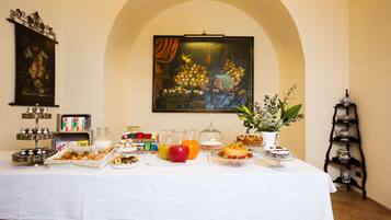 Un bufé de desayuno con diversas opciones de comida y bebidas, un cuadro en la pared y un juego de té sobre una mesita.