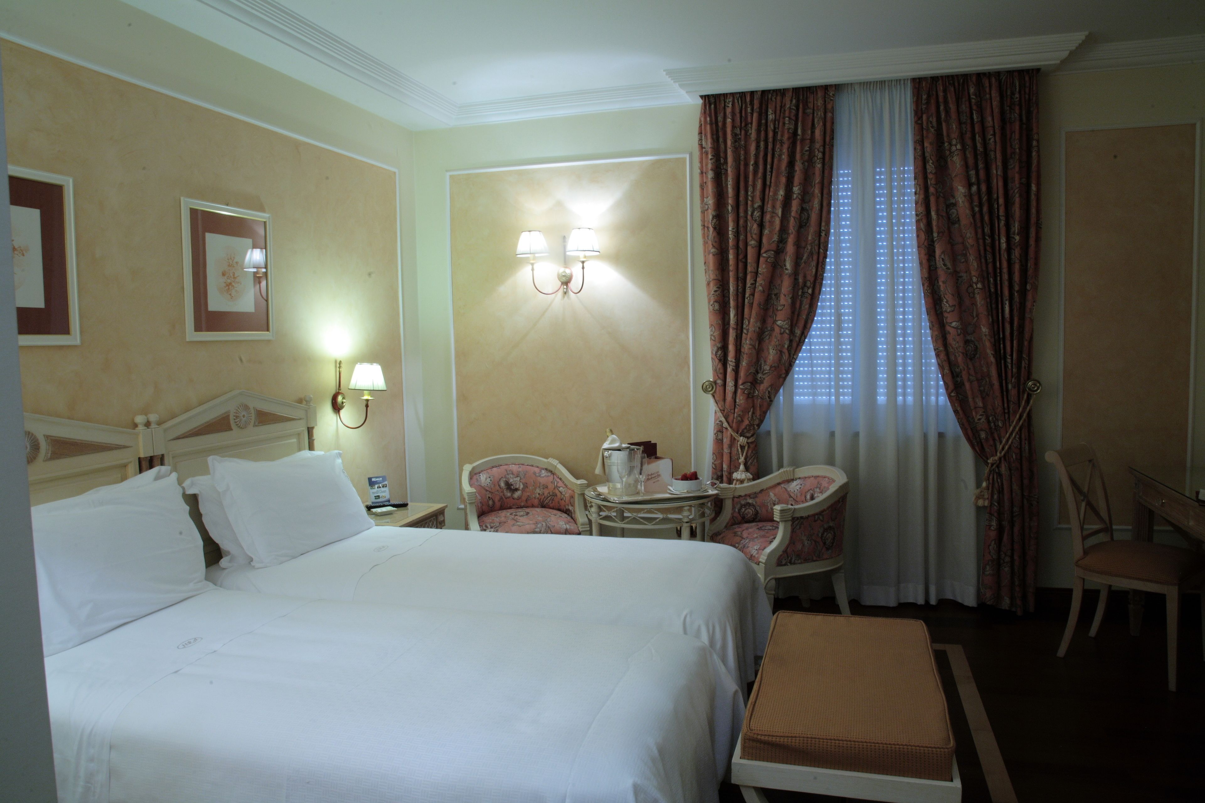 A hotel room with a large bed, two chairs, a small table with a lamp, and a window with curtains.