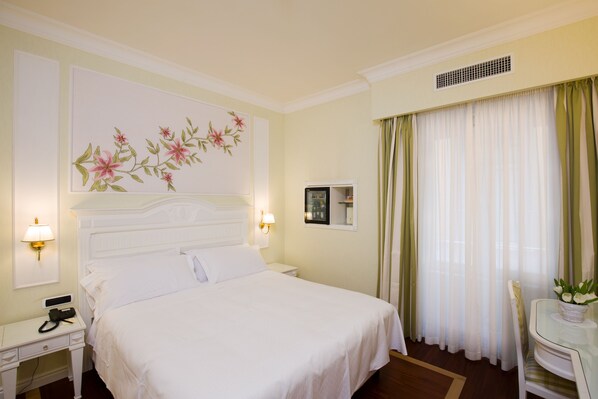 A hotel room with a large bed, bedside tables, a desk, and a chair. - Palazzo Alabardieri (Naples)