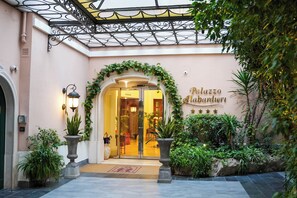 Entrada de un hotel con un balcón de hierro forjado, una puerta de vidrio y un letrero que dice "Palazzo Alabardieri".