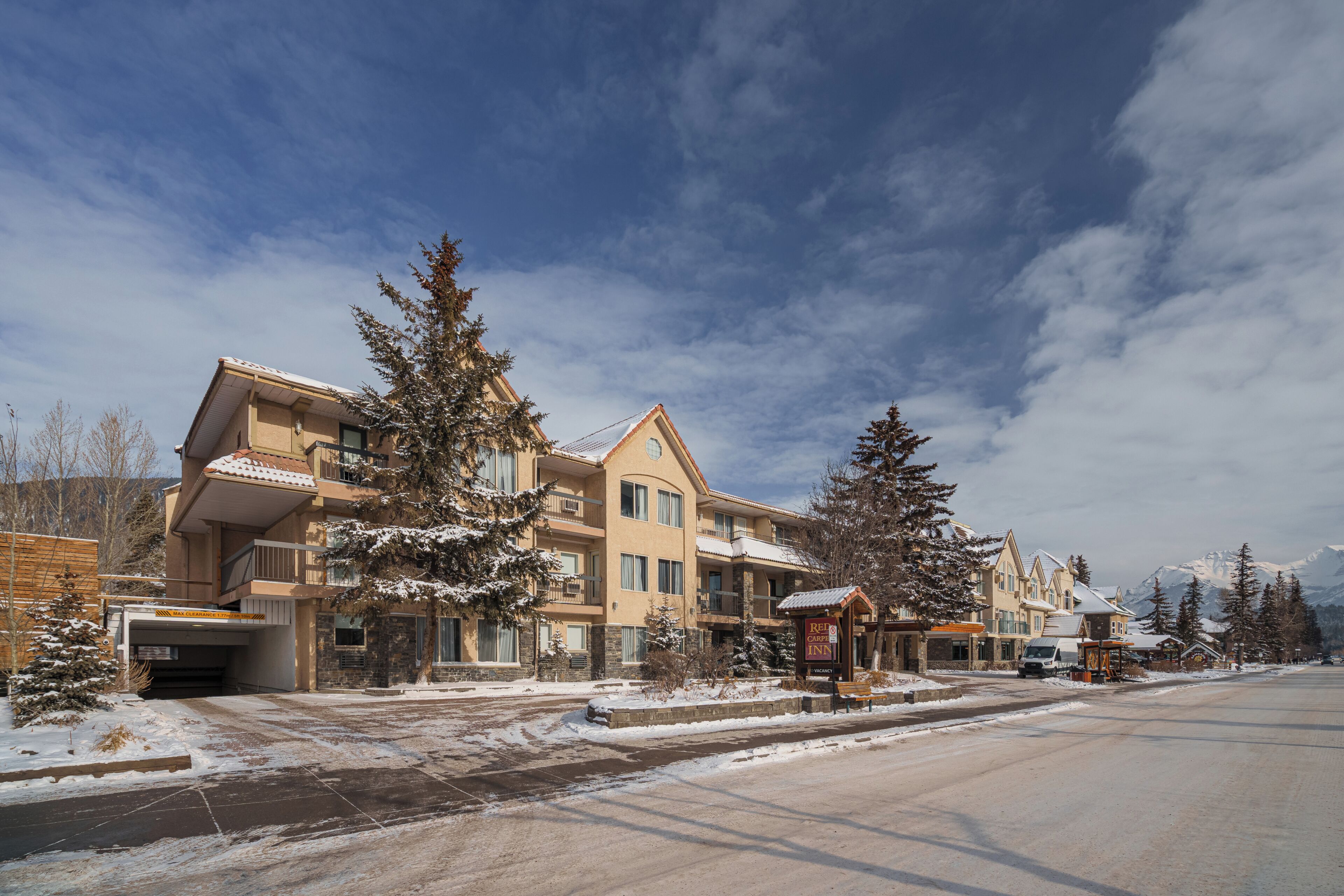 A multi-story hotel with a snow-covered landscape, a parking area, and a clear sky.