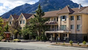 A hotel with a mountain backdrop, featuring a red carpet sign, a balcony, and a stone facade. - Red Carpet Inn (Banff)