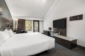 A hotel room with a large bed, a desk with a flat-screen TV, and a window with curtains.