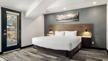 Un dormitorio moderno con una cama grande, cabecera de madera, dos lámparas de noche y vista a través de una puerta de cristal.