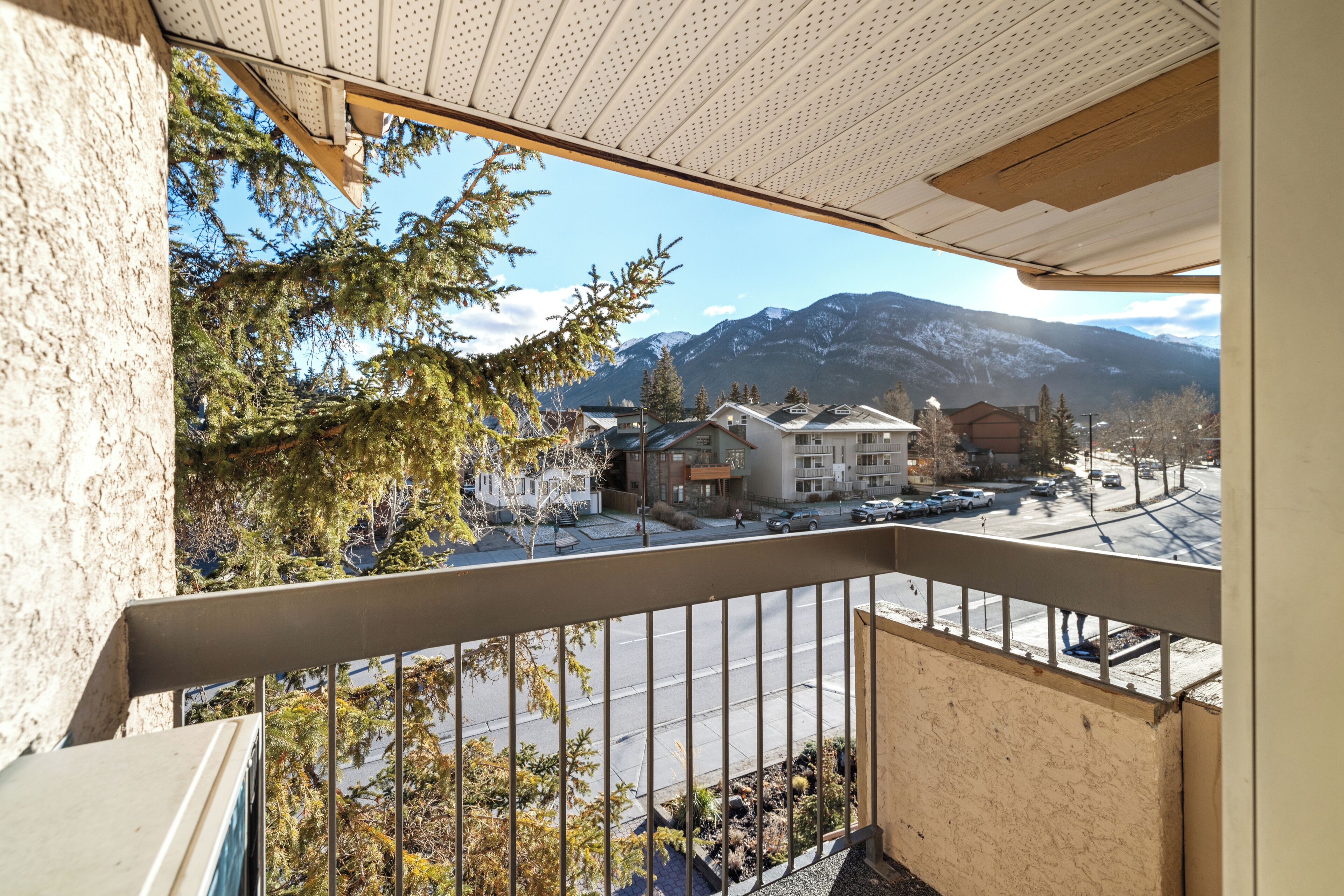 Un balcon offrant une vue sur une chaîne de montagnes, un parking et des bâtiments au style architectural moderne.