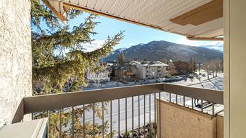 Un balcon offrant une vue sur une chaîne de montagnes, un parking et des bâtiments au style architectural moderne.
