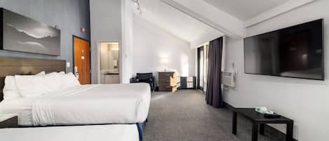 A hotel room with two beds, a flat-screen TV, a desk, and a large window.